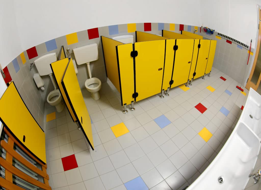 The photo shows clean toilet cubicles in a school bathroom.